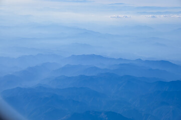 The view of the stunning landscape with mountains and clouds from the airplane window. Aerial view of the natural scene, mountain range. Travel and landscape scene. Travel and nature concept. 