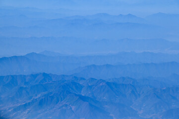 Fototapeta premium The view of the stunning landscape with mountains and clouds from the airplane window. Aerial view of the natural scene, mountain range. Travel and landscape scene. Travel and nature concept. 