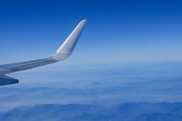 Looking from the airplane window with the airplane wing and the stunning landscape and blue sky. Mountains are under the airplane. Landscape, travel concept and nature scene. 