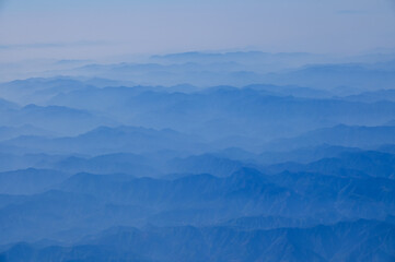 The view of the stunning landscape with mountains and clouds from the airplane window. Aerial view of the natural scene, mountain range. Travel and landscape scene. Travel and nature concept. 