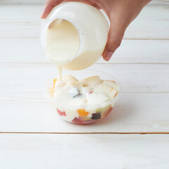 Fresh Fruit Salad With Creamy Dressing Being Poured Into a Plastic Bowl on a Rustic Wooden Table