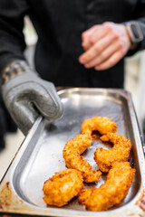 A chef wearing heat-resistant gloves holds a tray with perfectly fried shrimp. The golden-brown shrimp are crispy, showcasing a delicious appetizer ready to be served.