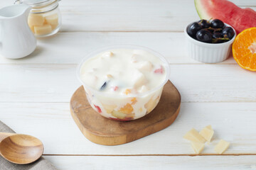 Refreshing Fruit Salad in a Plastic Bowl Garnished With Assorted Fruits, salad dressing and grated cheese and Yogurt at a Bright Kitchen Setting