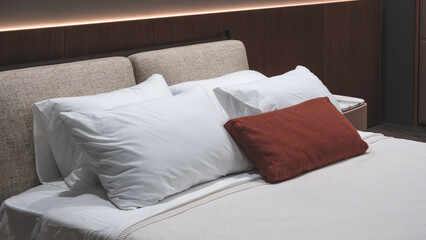 A bed with two white pillows and a red pillow. The bed is made and the pillows are neatly arranged. The bed is in a room with a wooden wall