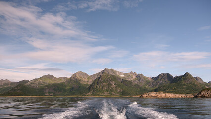 Boat leaving a trace on the water. The water is calm, in the background is a rocky island, Norway, Lafoten Islands, tourism travel concept background
