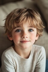 Young boy with light brown hair and blue eyes gazing thoughtfully indoors