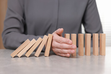 Woman stopping wooden blocks from falling at table, closeup. Domino effect