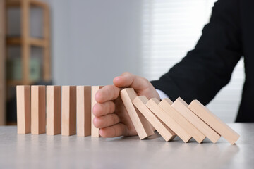 Man stopping wooden blocks from falling at table, closeup. Domino effect