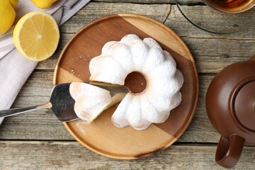 Delicious lemon cake with powdered sugar and citrus fruits on wooden table, flat lay