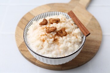 Delicious rice pudding with cinnamon and cashew nuts on white tiled table, closeup