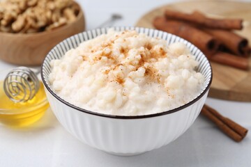 Tasty rice pudding with cinnamon served on white tiled table, closeup