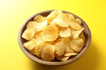 Tasty potato chips in bowl on yellow background, closeup