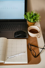 Home office desk workspace with laptop, coffee cup, blank sheet notebook, glasses and green plant 