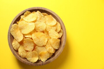 Tasty potato chips in bowl on yellow background, top view. Space for text