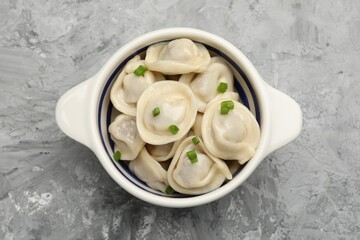 Delicious dumplings (pelmeni) with green onion in bowl on grey table, top view