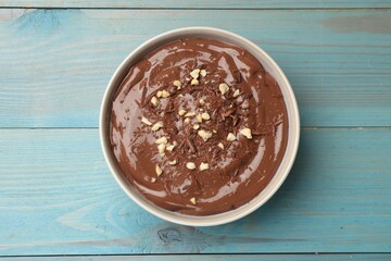 Tasty chocolate pudding in bowl on light blue wooden table, top view