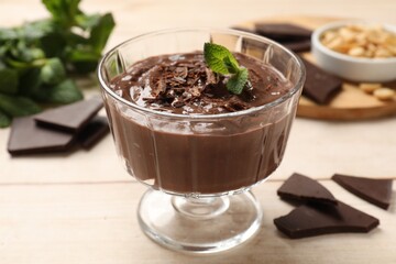 Tasty pudding with mint and pieces of chocolate on white wooden table, closeup