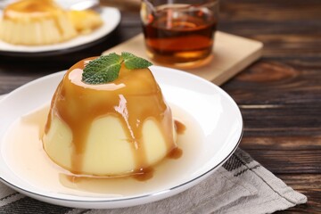Delicious pudding with caramel sauce and mint on wooden table, closeup