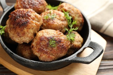 Tasty patties and dill in frying pan on wooden table, closeup
