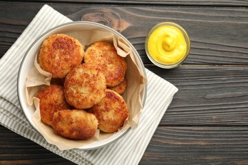 Tasty patties in bowl and mustard on wooden table, flat lay