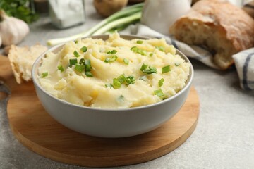 Delicious mashed potato with green onions served on grey table, closeup