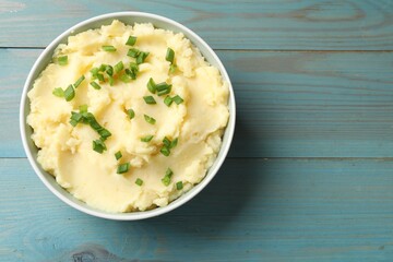 Delicious mashed potato with green onions in bowl on light blue wooden table, top view. Space for text