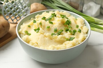 Delicious mashed potato with green onions in bowl on white marble table, closeup