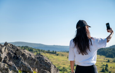 Naklejka premium Young Woman taking selfie pictures with her phone in the Summer Mountain 