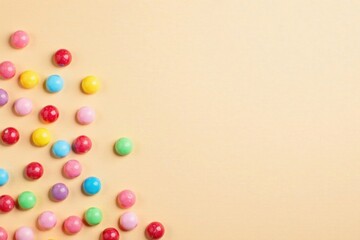 Obraz premium Colorful Spherical Candies Scattered on a Pale Yellow Background, Perfect for a Festive or Playful Design