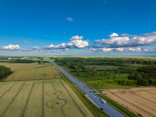 Aerial view of a rural landscape in Estonia, featuring golden wheat fields, a curving road, and unique crop circles. A scenic countryside shot perfect for agriculture, nature, and travel concept