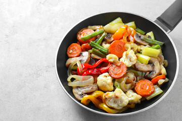 Different vegetables and mushrooms in frying pan on grey table, closeup. Space for text