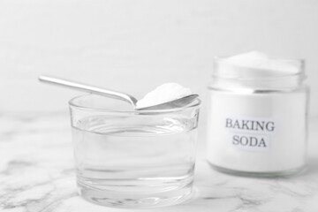Glass of water and baking soda on white marble table, selective focus