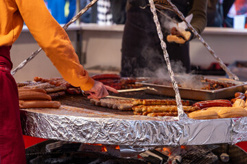 The vendor in an apron arranges the sausages alongside fresh bread rolls, showcasing local culinary tradition and a vibrant festival atmosphere.