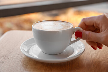 Woman with cup of aromatic coffee at wooden table in cafe, closeup