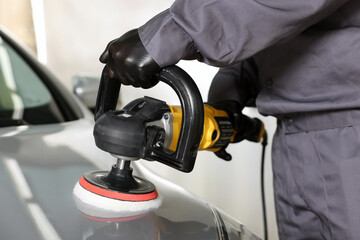 Man polishing car hood with orbital polisher indoors, closeup