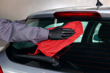 Man polishing car rear window with red rag indoors, closeup