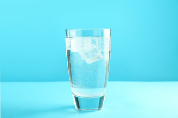 Soda water with ice cubes in glass on light blue background