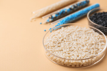 Colorful plastic granules in petri dishes and test tubes on beige background, closeup. Space for...