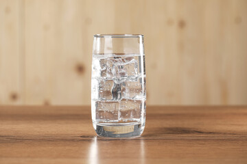 Refreshing soda water with ice cubes in glass on wooden table