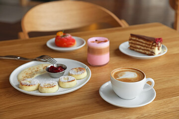 Delicious cottage cheese pancakes, desserts and aromatic coffee served on wooden table in cafe
