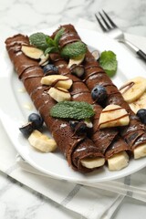 Delicious chocolate crepes with banana and blueberries served on white marble table, closeup