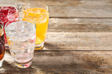 Soda water of different flavors with ice cubes in glasses on wooden table, closeup. Space for text