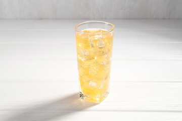 Sweet soda water with ice cubes in glass on white wooden table
