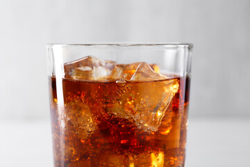 Sweet soda water with ice cubes in glass on blurred background, closeup
