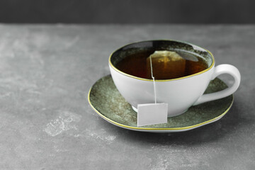 Tea bag in cup with hot drink on gray textured table. Space for text