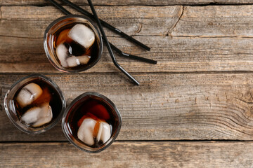 Refreshing cola with ice cubes in glasses and drinking straws on wooden table, flat lay. Space for text