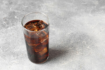 Refreshing cola with ice cubes in glass on light textured table, closeup. Space for text
