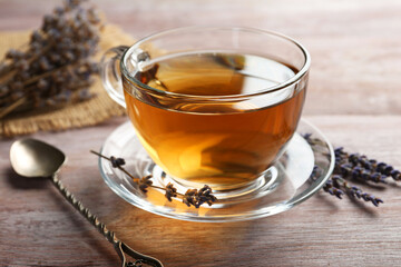 Aromatic lavender tea in glass cup, spoon and dry flowers on wooden table, closeup