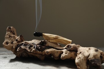Smoldering palo santo stick and snag on wooden table against grey background, closeup