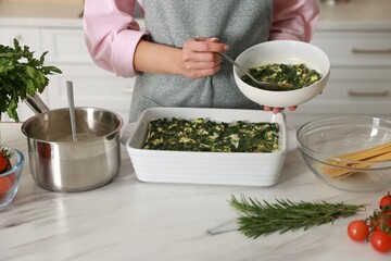 Woman making spinach lasagna at marble table indoors, closeup